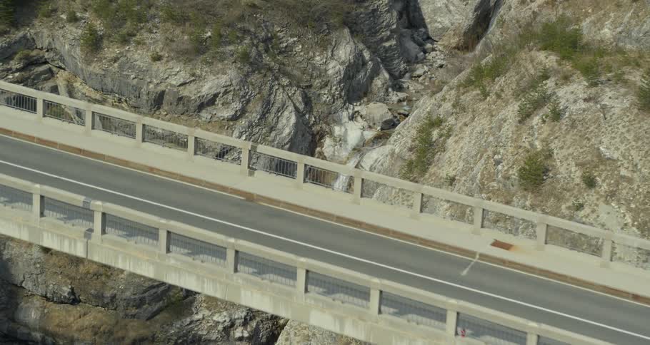 Concrete bridge stretching over a rocky gorge and a waterfall in the background