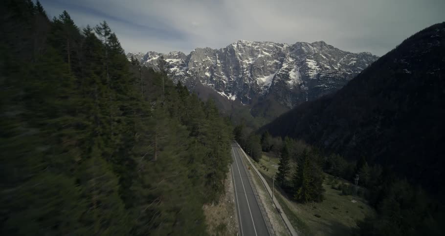 Road that winds through a valley flanked by snowy mountains and a partly cloudy sky