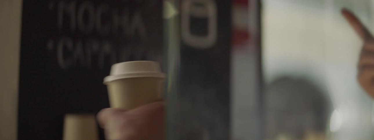 A human hand reaching for a cup of coffee to another person in a coffee shop