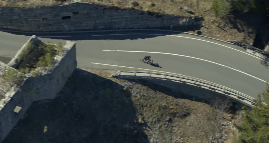 Asphalt road winding through a wooded area with a cyclist traveling along it