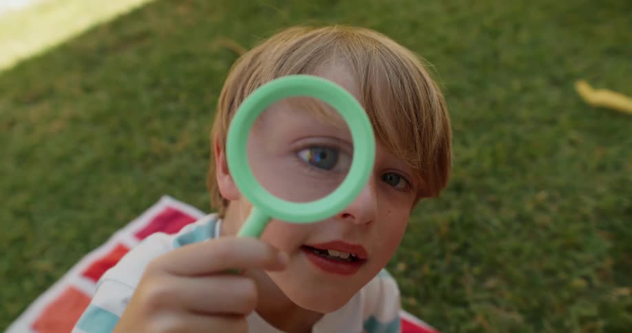 A little blond boy who has a magnifying glass in his eye and the image of his eye is big