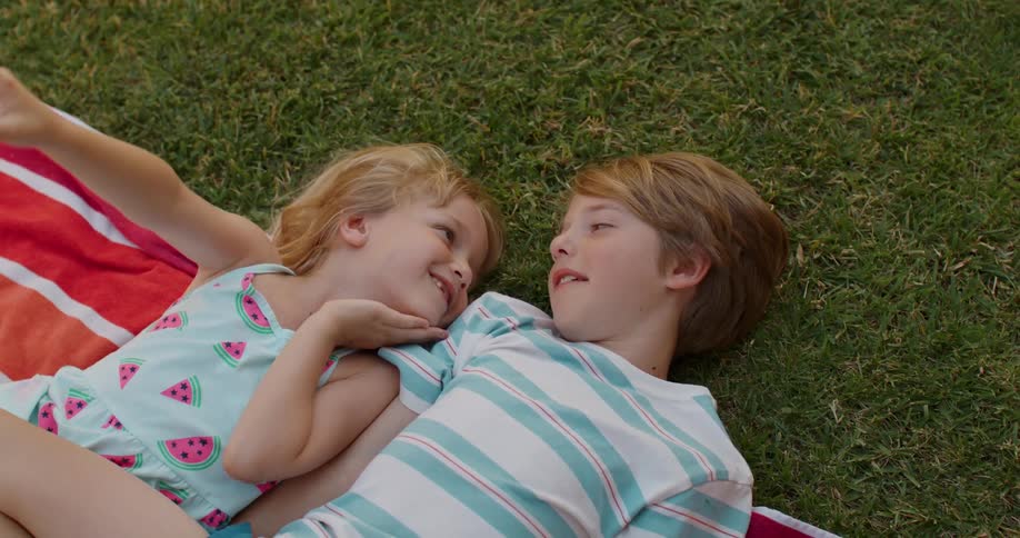 A brother and sister talk while laying in the grass