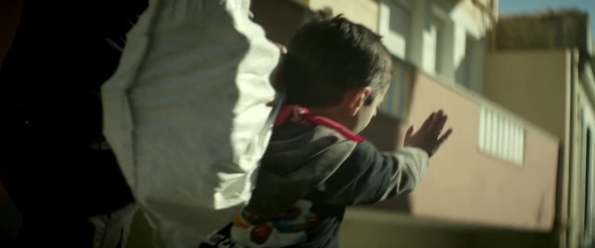 A small child walking with an adult carries a sack over his shoulder