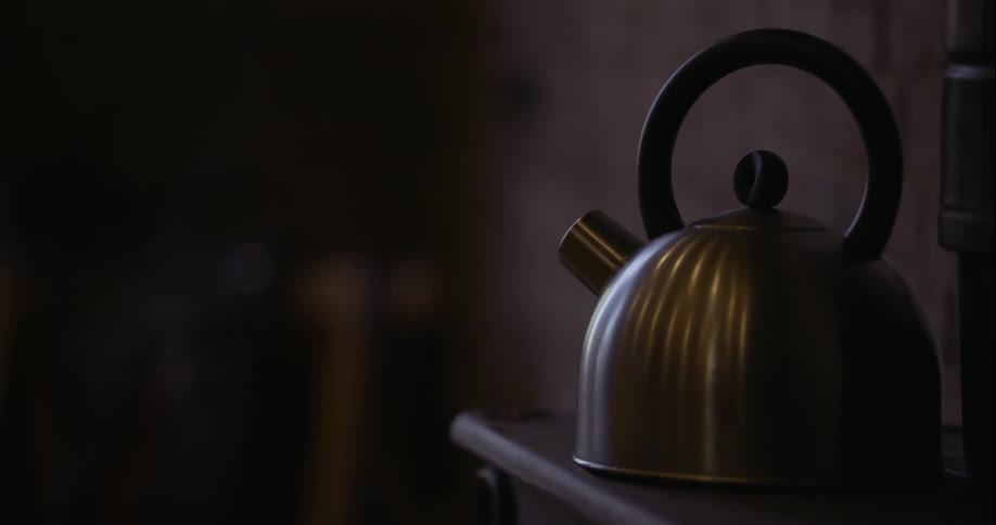 Old-fashioned tea kettle sitting on a stove in a dark setting