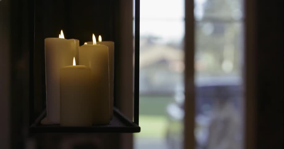 Candles flicker near a window as people walk by