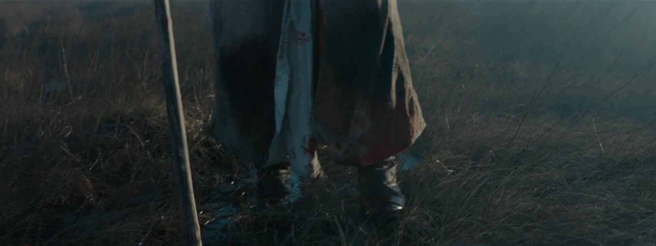 Person with a staff walking on wet dry grass