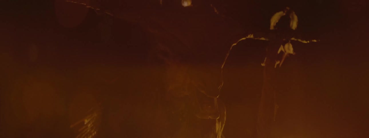 The skull of a horned animal hanging from sticks surrounded by sparks from a fire at night