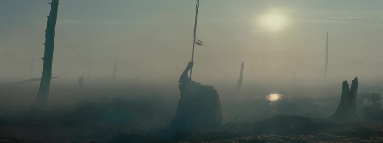 Person walking with a spear and falling to the ground in a swamp  with fog and the sun on the horizon