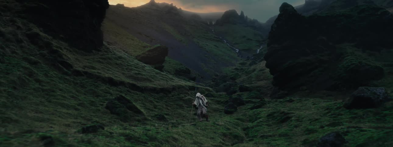 Person with a staff walking through a green valley