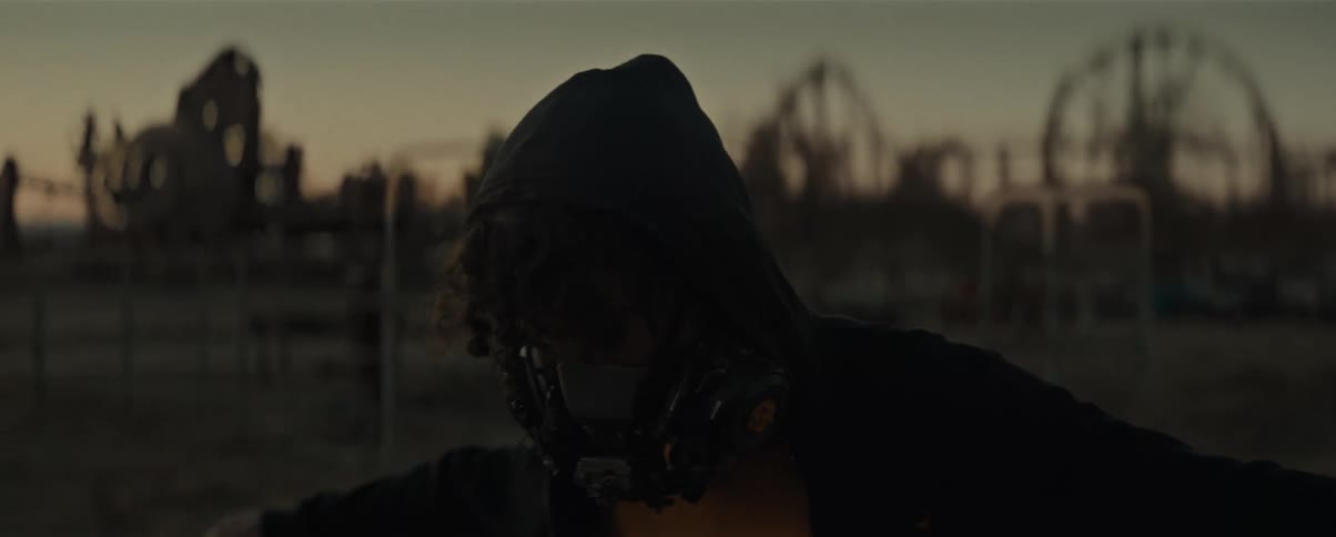Person with a mask and hood walking in a field in the late afternoon