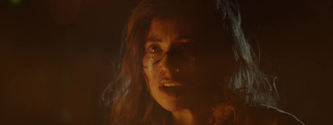 Close up of the face of a woman with war paint on her face talking near a fire at night