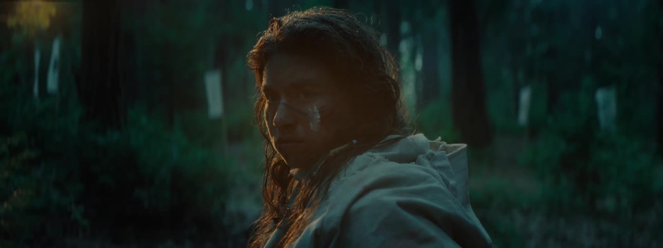 A native american with long hair gazes into a forest during twilight