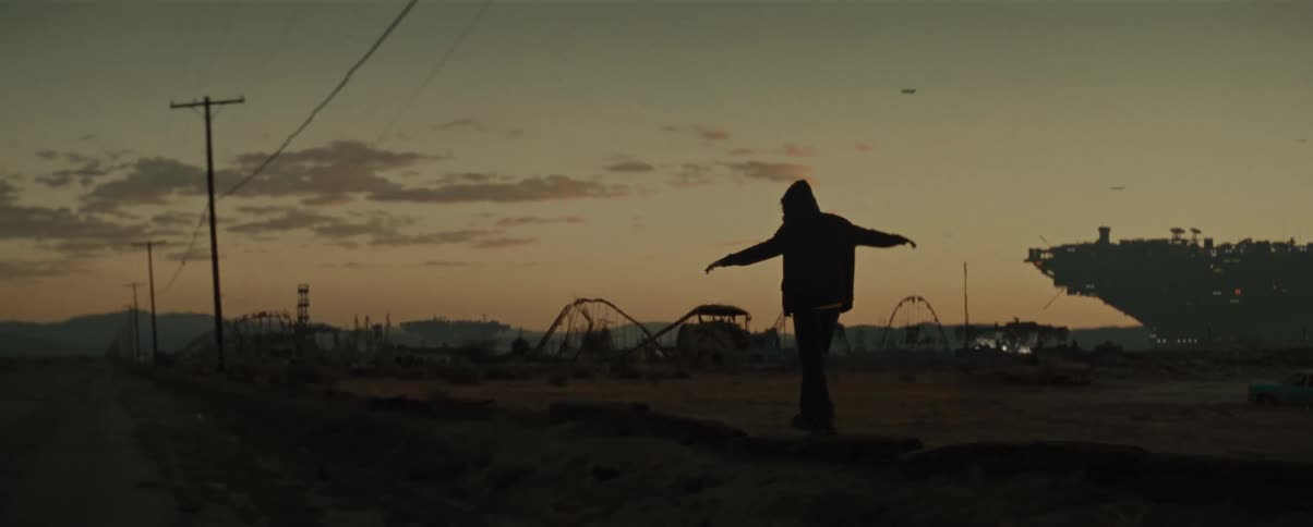 Silhouette of a person walking across cement step on a field of an abandoned amusement park at dusk