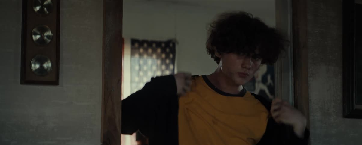 Teenager with messy hair standing on a door frame at home puts on a sweater
