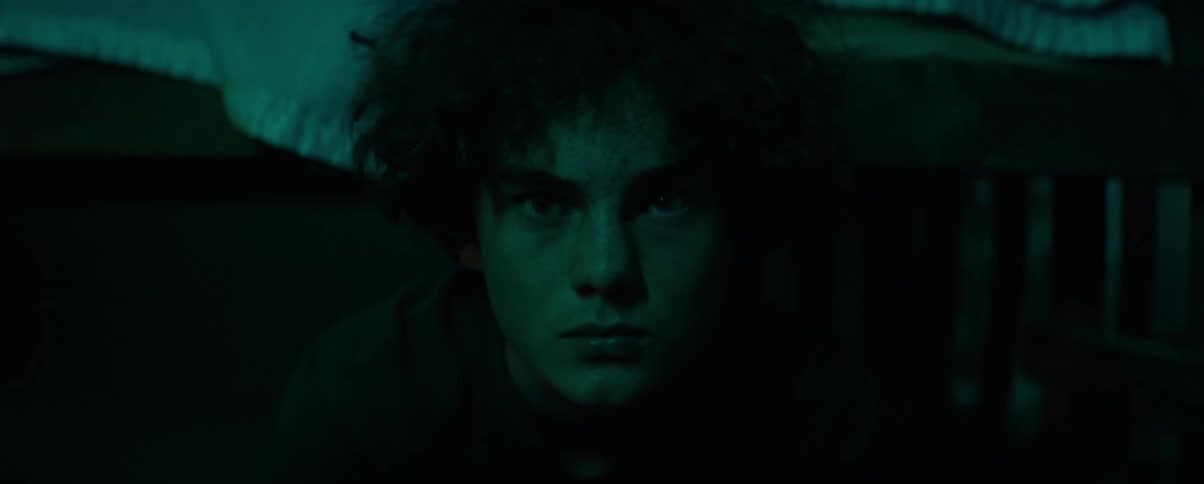 Male teenager sits in dark bedroom glaring