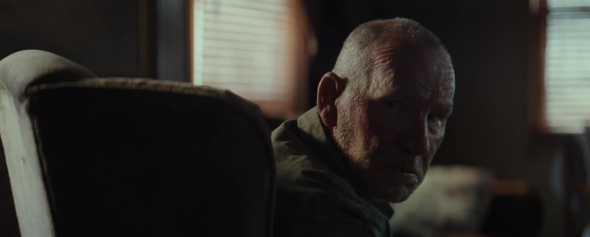 Elderly man sitting in a living room looks to the side with a frown