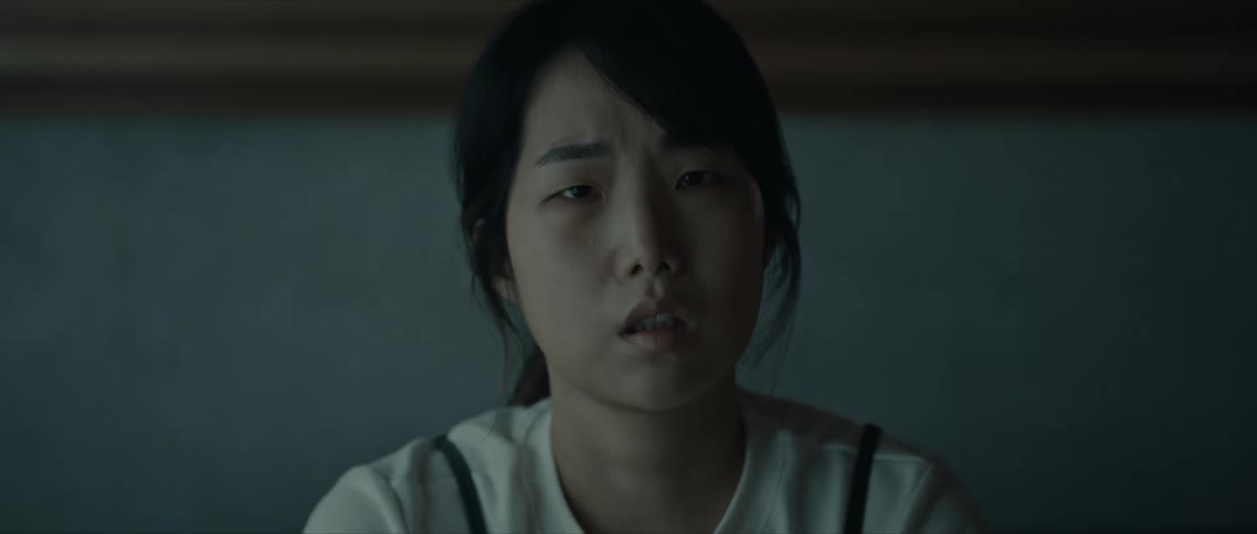 A young woman with dark hair stares into the distance with a worried expression