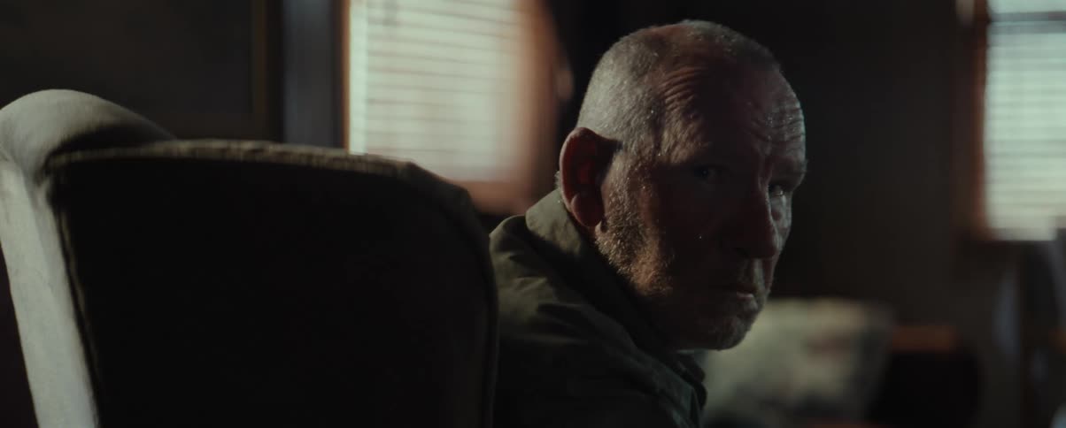 An elderly man with wrinkles on his face turns around slowly to look at the camera