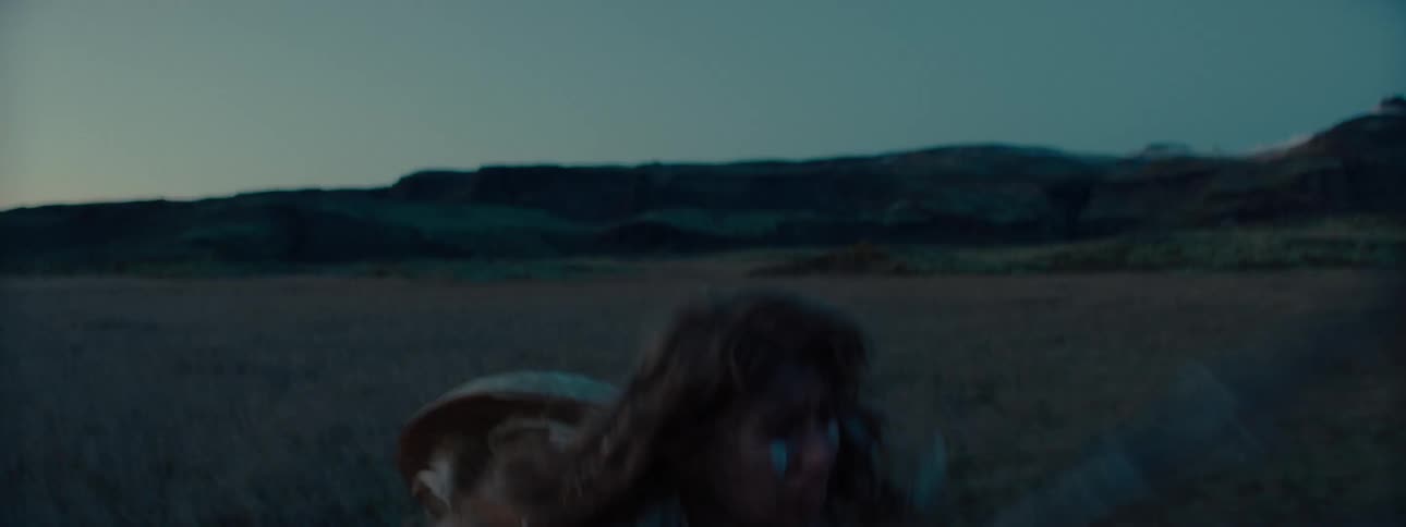 A woman runs through a grassland in fear stumbling as she does