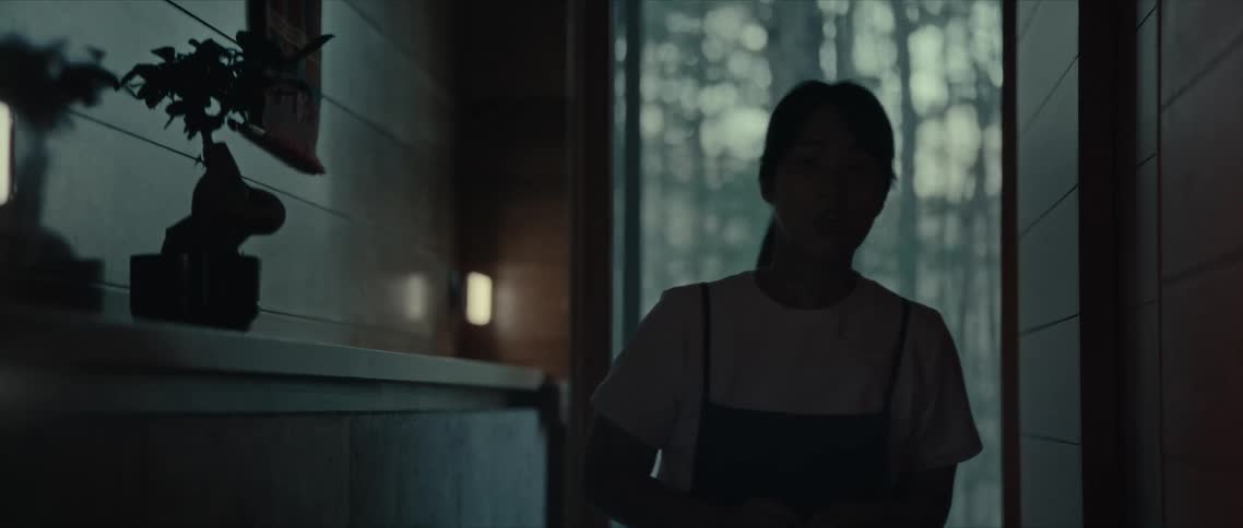 Woman wearing an apron hesitantly walks through a dimly lit room