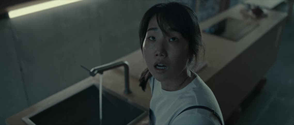 Young asian woman in the kitchen in front of the sink with fear facial expression