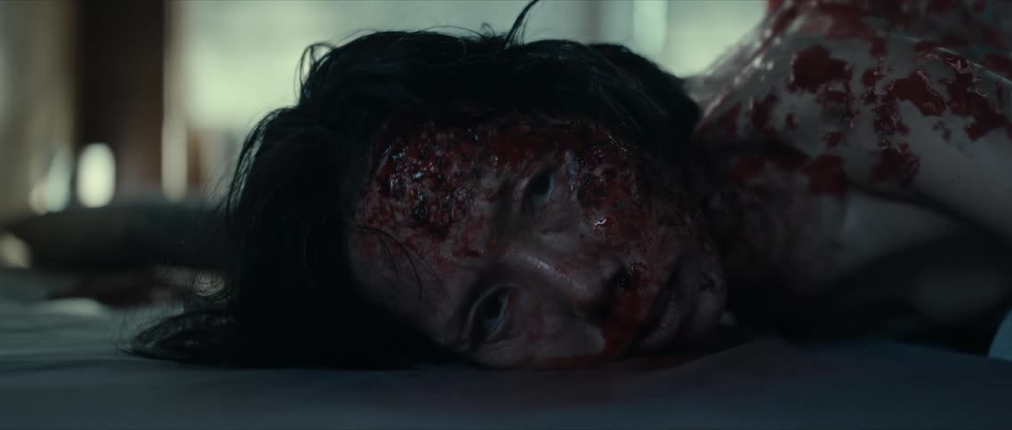 A horror scene of woman covered in blood laying down on a bed