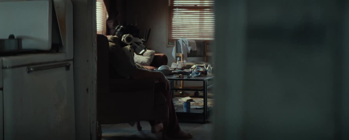 A man wears a vr headset while sitting in a cluttered living room in a rundown house