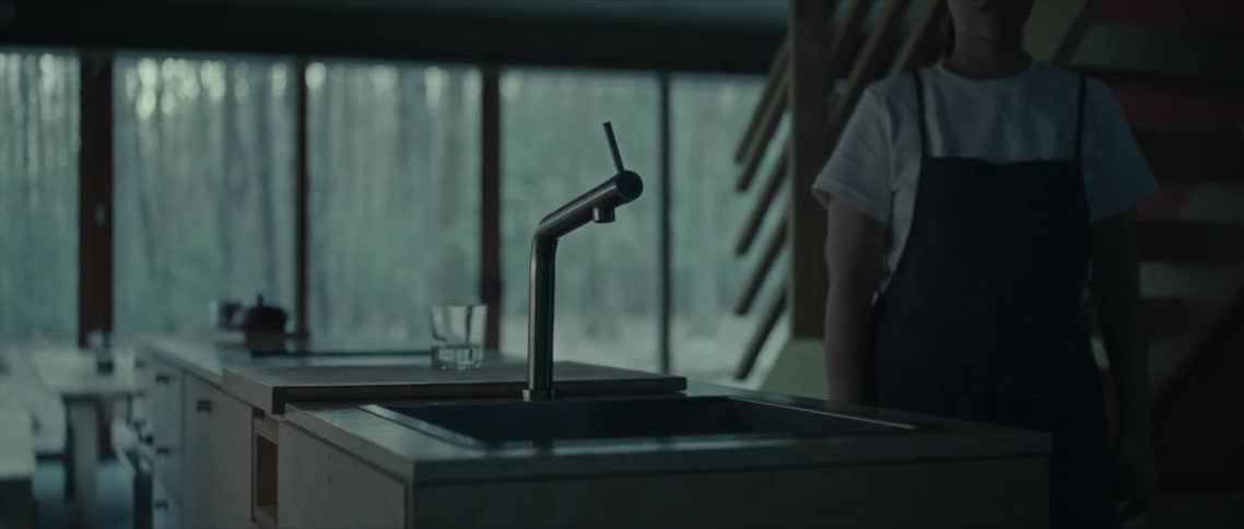 A woman arriving in a kitchen and opening the tap and letting water run into the sink