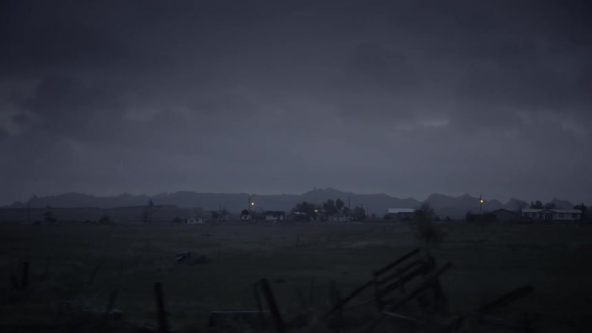 Houses in rural areas against a cloudy sky and the silhouette of mountains on the horizon