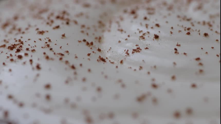 Extreme close up on a white cream with a brown powder falling down