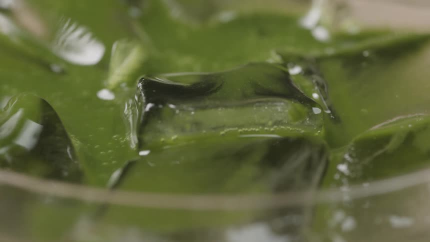 Closeup on a greenish viscous liquid in a glass with ice in a straw