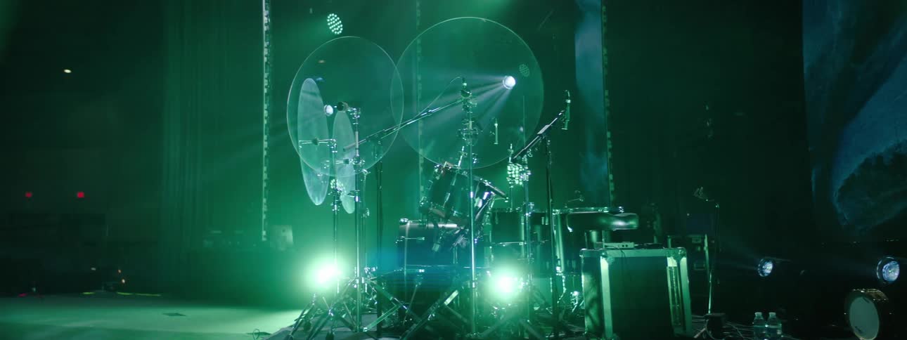 Drum set with cymbals drums and pedals mounted on a stage illuminated by green lights