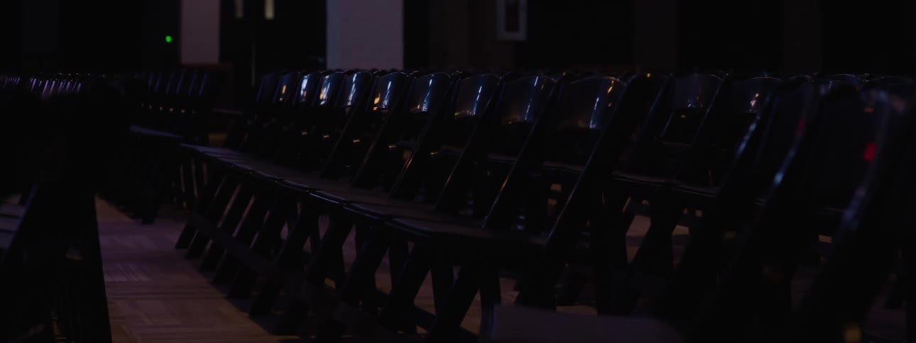 A row of empty black chairs neatly arranged in a dimly lit room