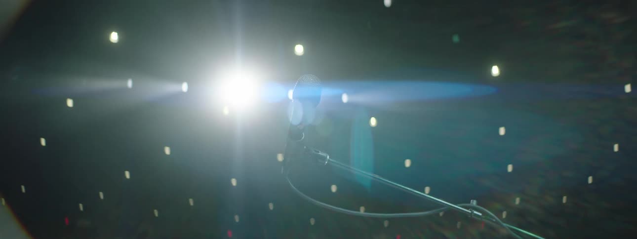 A black microphone on a stage with spotlights shining brightly behind