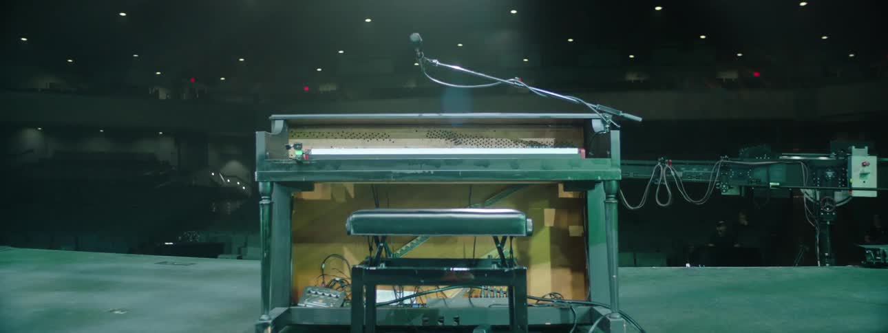 Stage with a piano and a bench in the center lit by soft lights in front of a large empty concert hall