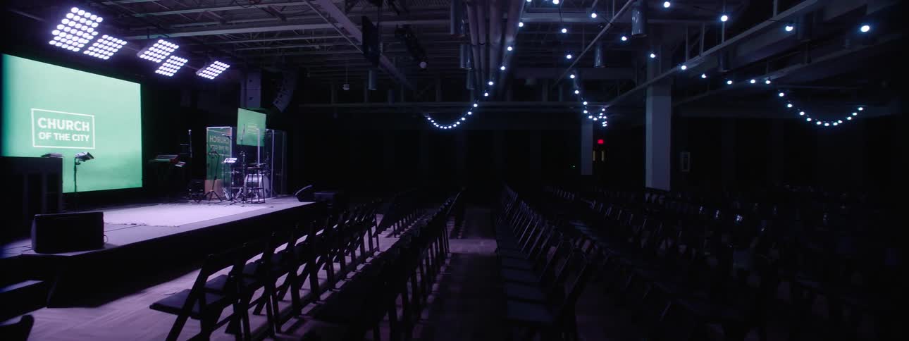 A church theater with a stage with monitors and instruments and strings of lights hanging over seats