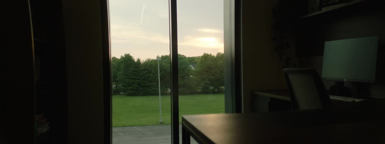 A oneroom glass window overlooking a green lawn with trees