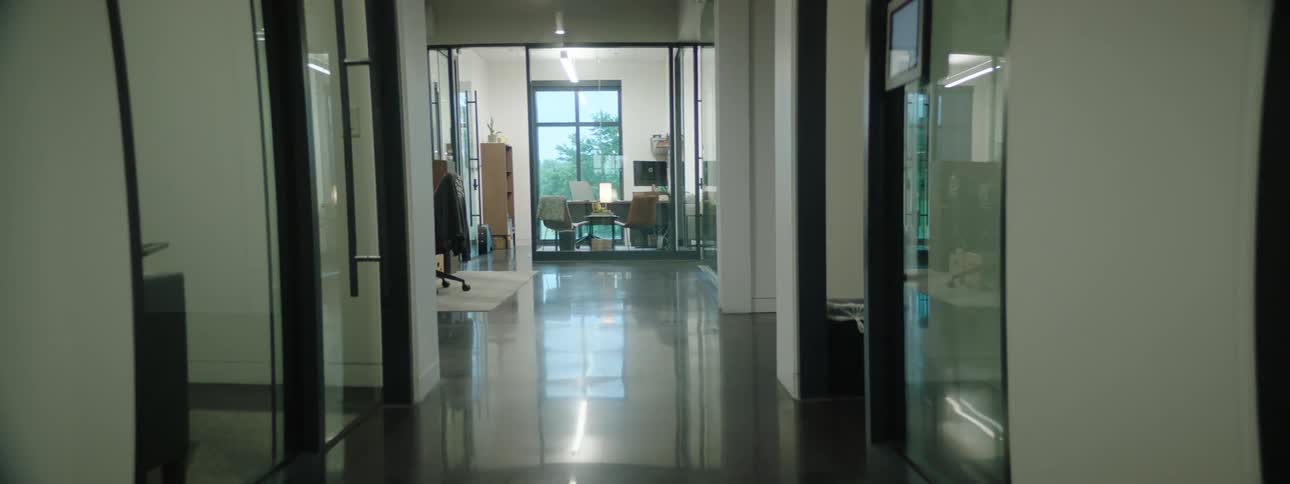 An interior with a hallway with some glass doors and the floor is reflecting the environment