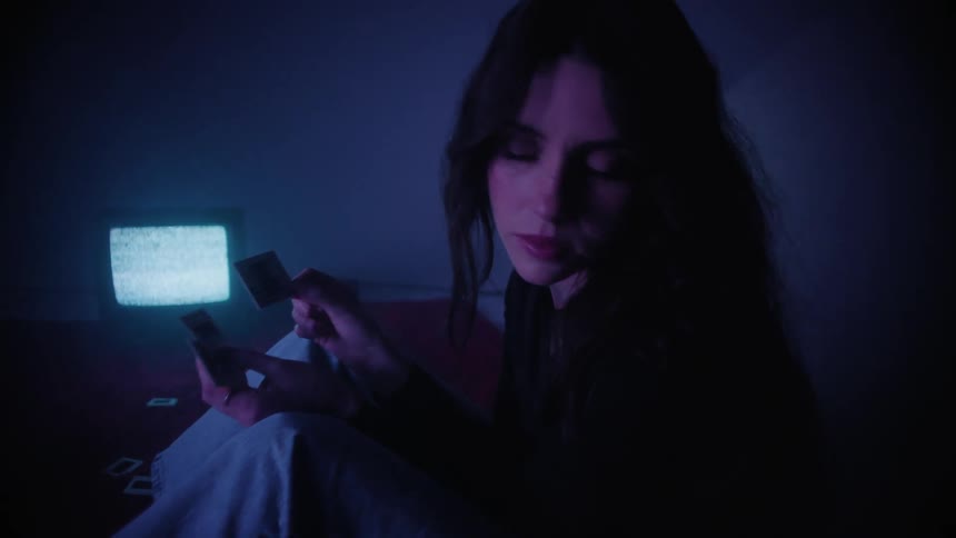 A woman shaking and looking at two photography negatives while a tv plays static in the background
