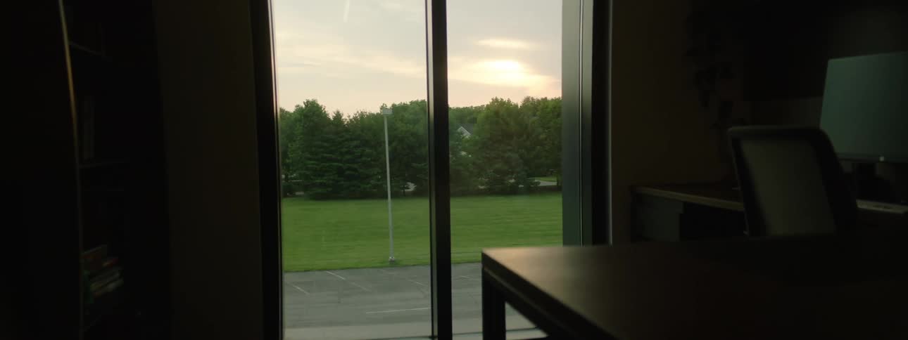 Interior of an office with a desk and computer monitor on the right with a window overlooking a twilight
