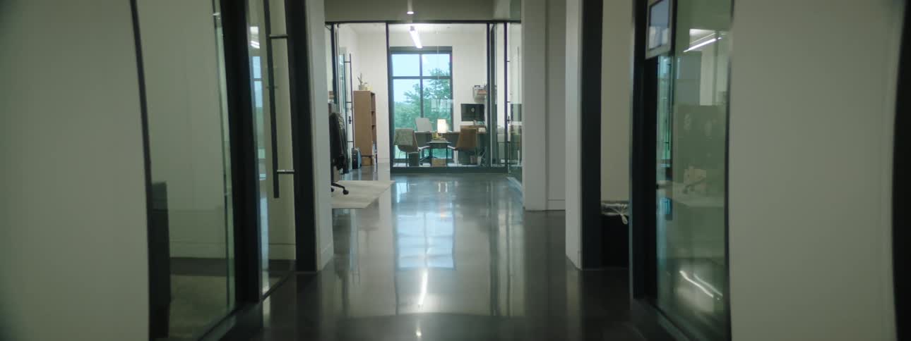 An empty office hallway opens into an office with desks and filing cabinets