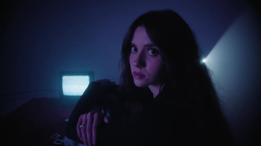 Young woman sitting on a rug in a dark room with a neon light and books around