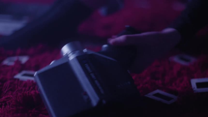 A person is sitting on a red carpet with several photos on the floor and he takes out a camera