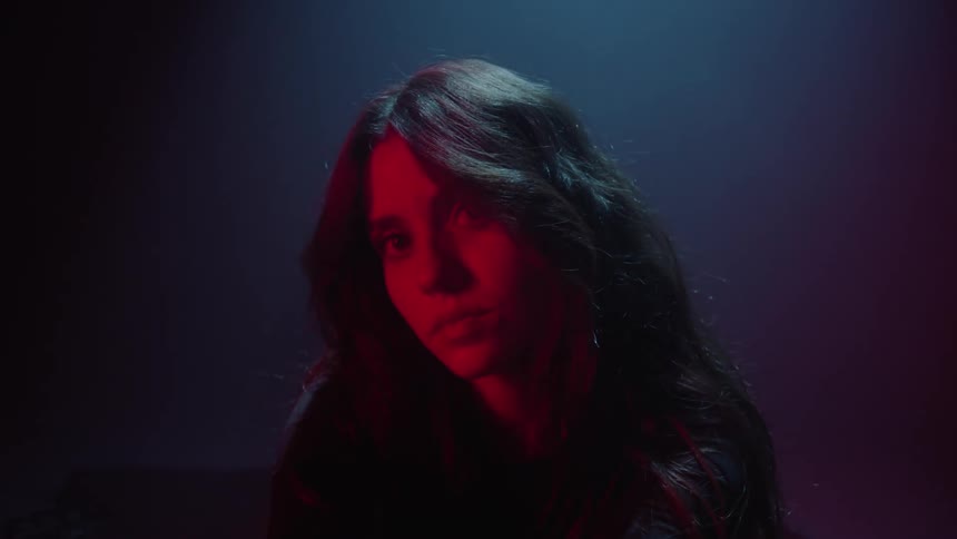 The face of a young woman that is illuminated by a red light and there is a white light coming from above that is illuminating the room