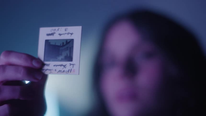 Woman holding a small polaroid photo in a dark room with a neon light in the background