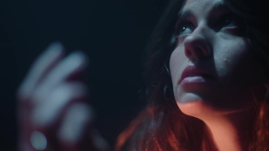 Close up of a young woman looking around inside a dimly lit room with moody light