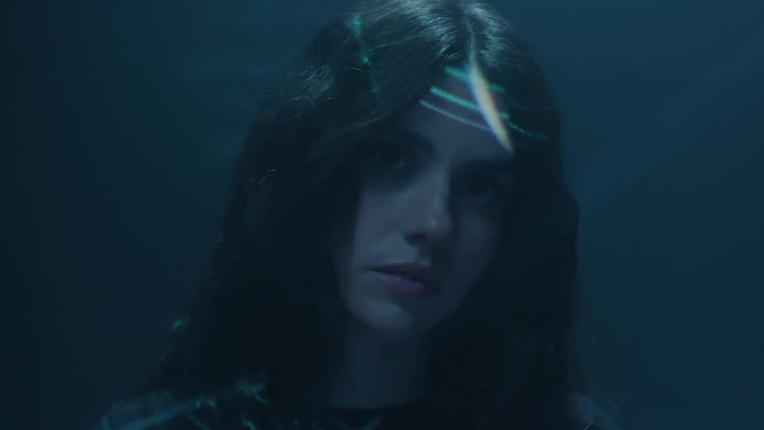 Young woman sways in placein a dimly lit area as a projected light grid passes over her face