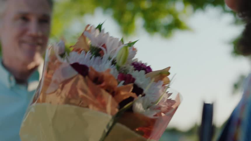 A man gives a woman a bouquet of flowers on a sunny day