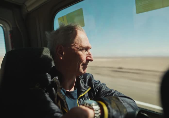 Old man looking out a large window in a van as it drives through the desert