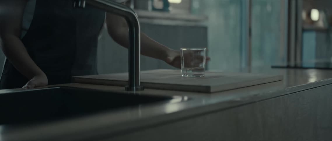 A young woman wearing an apron places a glass of water over the kitchen countertop
